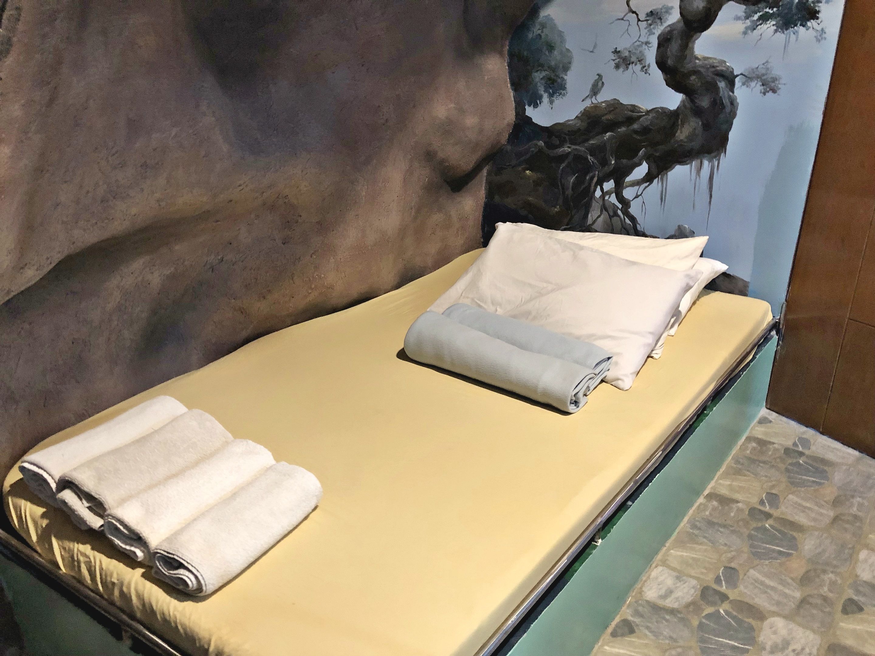 Una cama con colchón amarillo, almohadas blancas y toallas dobladas.