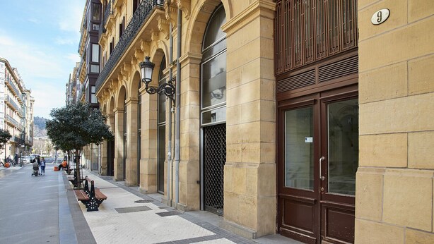Calle con un edificio que tiene ventanas amplias, una reja de metal y un letrero con el número 9.