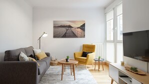 Una sala de estar moderna con sofá, sillón, televisor y un cuadro de una escena costera.