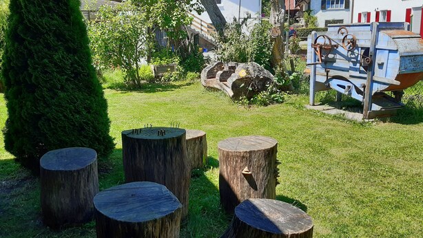 A garden with wooden stumps, a tall tree, and a rustic outdoor seating area. - Vacation home on the romantic road (Landsberg/Erpfting)