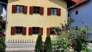 A building with a textured facade, multiple windows with shutters, and a metal fence in front. - Vacation home on the romantic road (Landsberg/Erpfting)