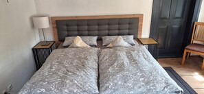 A double bed with a grey upholstered headboard, two bedside tables with lamps, and a wooden chair.