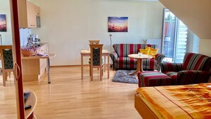Una sala moderna con sofá, una mesita y una cama. Incluye una zona de cocina con alacenas y una máquina de café.