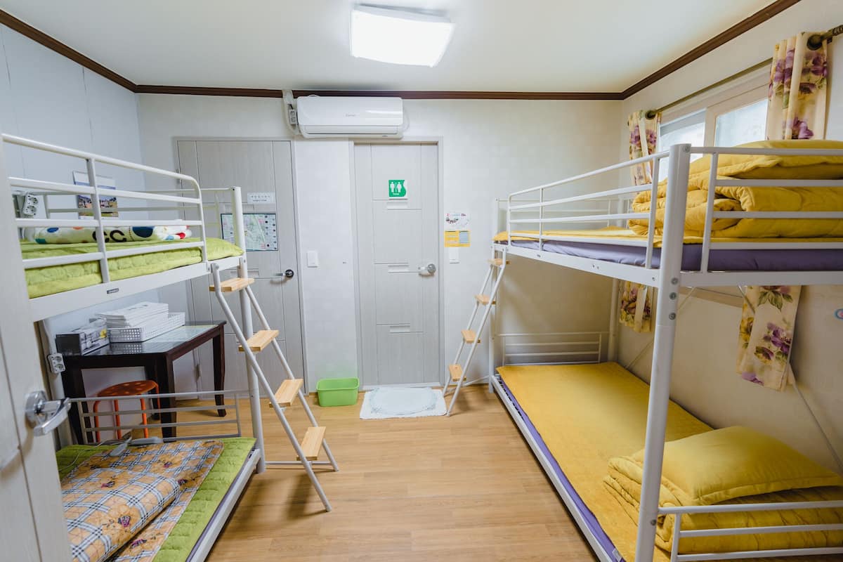 A dormitory room with bunk beds, a desk, and a door with an emergency exit sign.