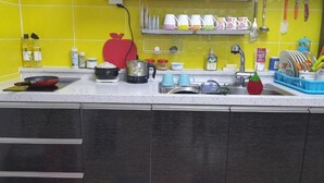 Una cocina con salpicadero amarillo, un recipiente rojo con forma de manzana y distintos utensilios y electrodomésticos.