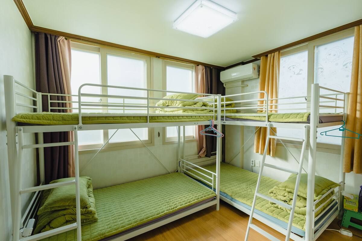 A bunk bed room with three levels, a window with curtains, and a ceiling light.