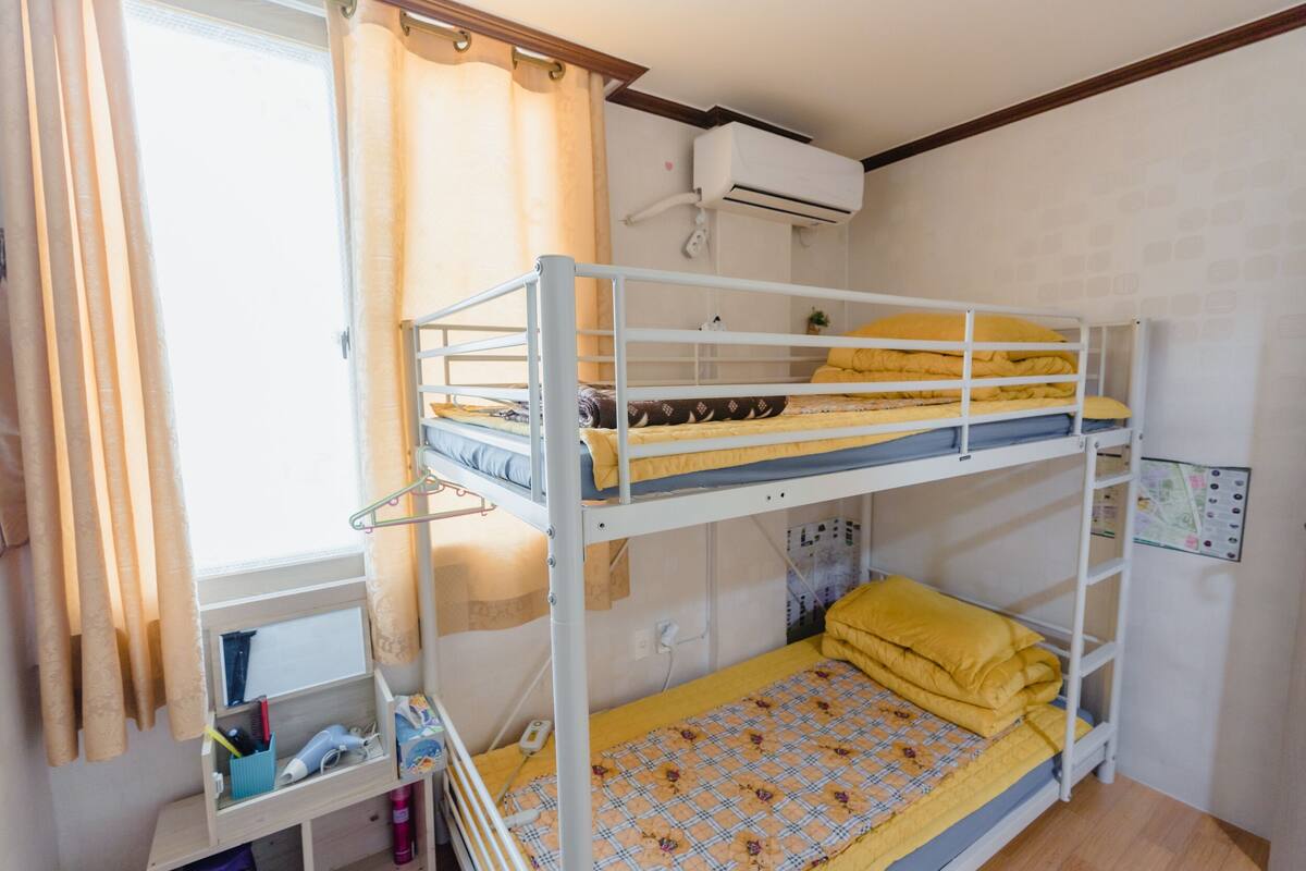 A bunk bed room with a window, curtains, and an air conditioning unit.