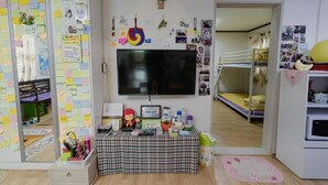Habitación infantil con televisor, cama, escritorio lleno de juguetes y una pared decorada con notas y dibujos.