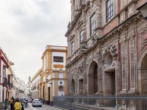 Uma rua com edifícios históricos, incluindo um com arquitetura elaborada e fachada amarela.