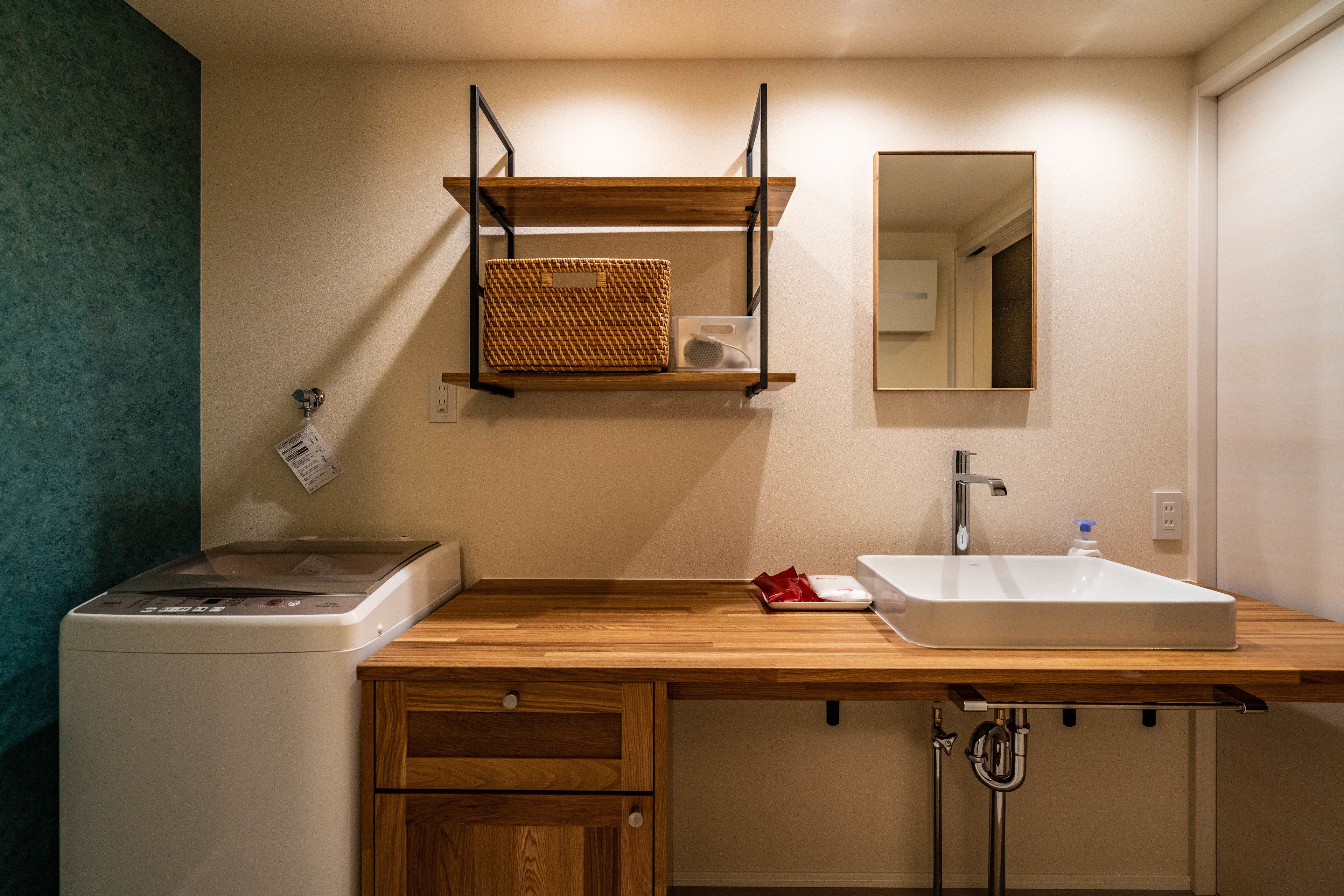 A compact bathroom with a washing machine, wooden countertop, sink, and a mirror.