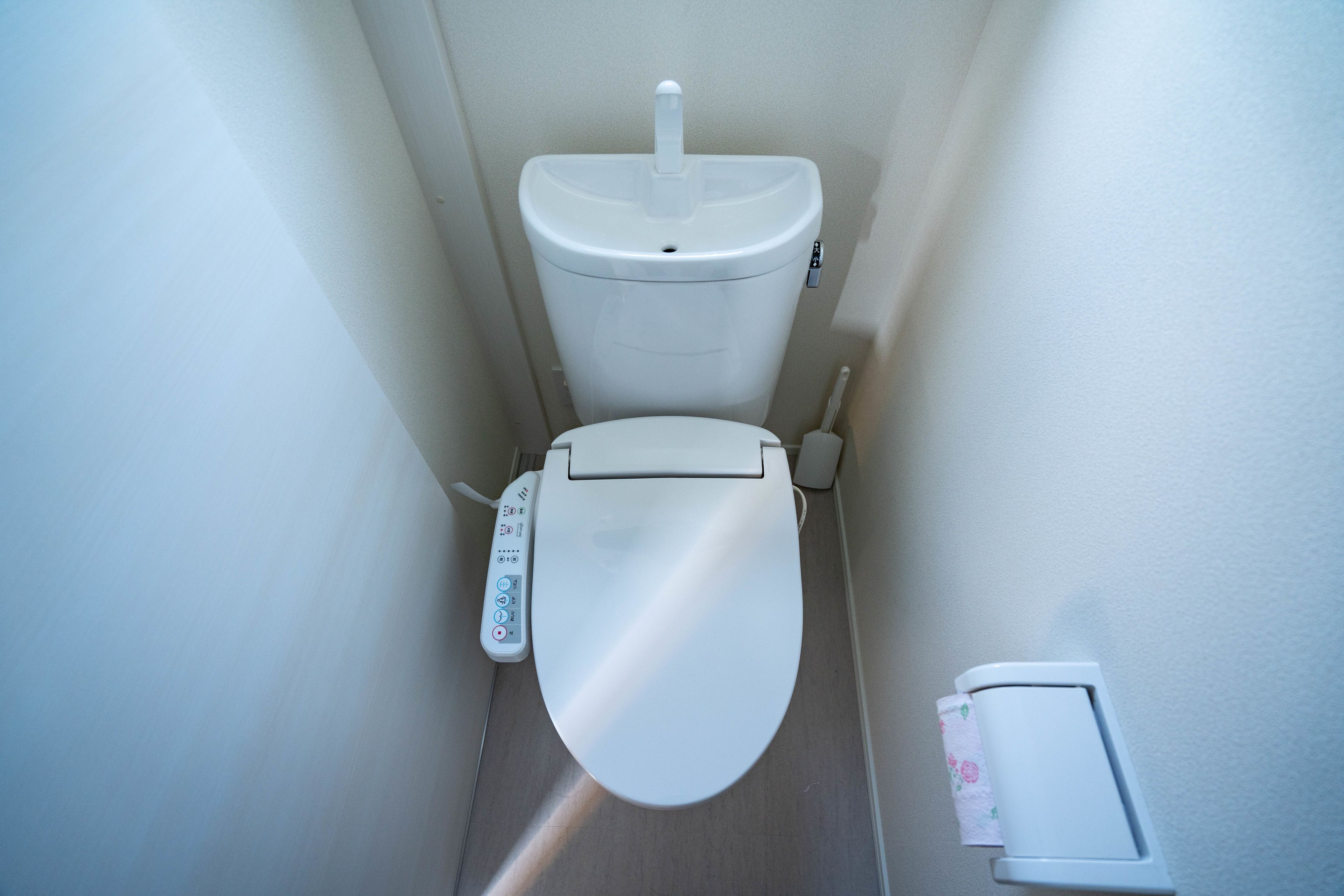 A small, modern bathroom with a toilet, a flush handle, and a toilet paper holder.