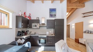 A compact kitchen with modern appliances, a dining area with a table and chairs, and a living area with a sofa and a fireplace.