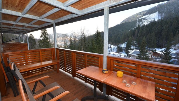 A wooden deck with benches and a table, overlooking a snowy mountain landscape.