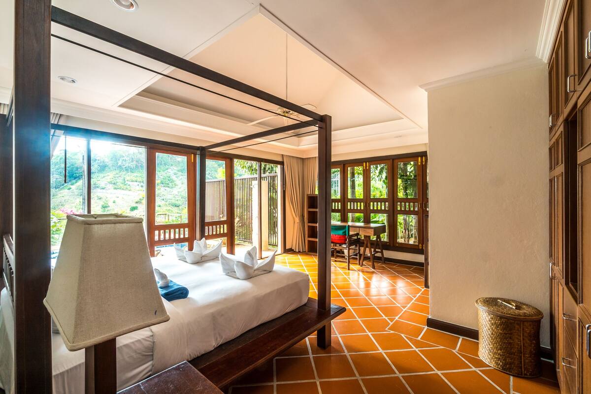 A bedroom with a four-poster bed, a bedside lamp, and a view of the outdoors.