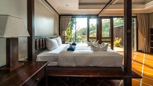 A four-poster bed with white linens, a wooden nightstand, and a view of a garden through large windows. - Nakatani Villas By Lofty (Kamala)