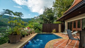 A swimming pool with tiled edges, surrounded by potted plants and a patio area with chairs and a table. - Nakatani Villas By Lofty (Kamala)