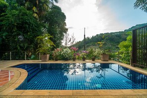Una piscina con bordes de azulejos, rodeada de plantas en macetas y árboles.