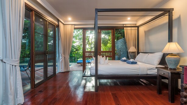 A spacious bedroom with a four-poster bed, a nightstand, and a view of the outdoors. - Nakatani Villas By Lofty (Kamala)