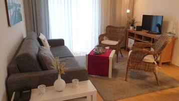 Ein gemütliches Wohnzimmer mit einer Couch, zwei Korbstühlen, einem Couchtisch und einem Fernseher.