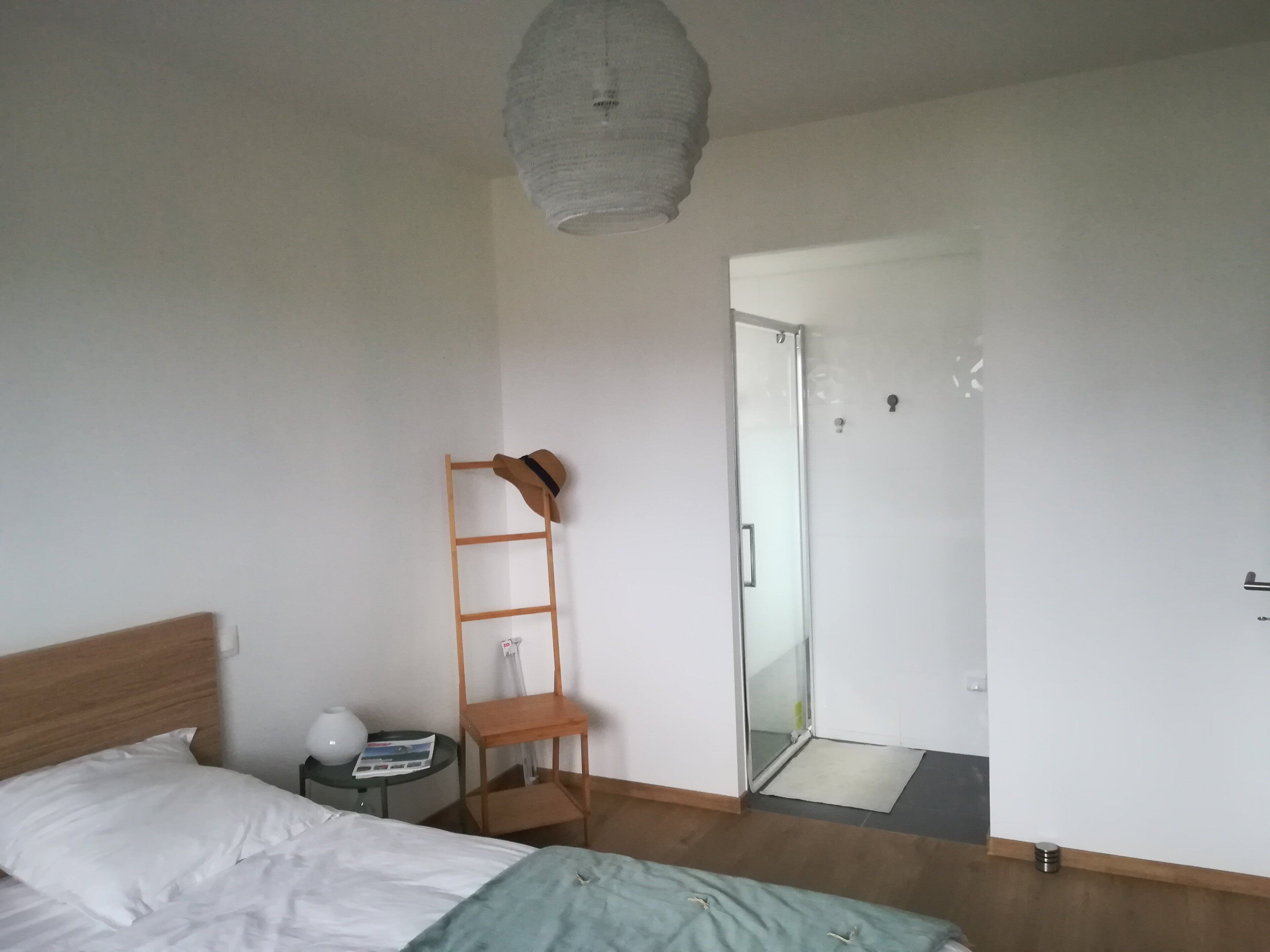 A bedroom with a bed, a nightstand, a small table with a lamp, a ladder, and a door leading to a bathroom.