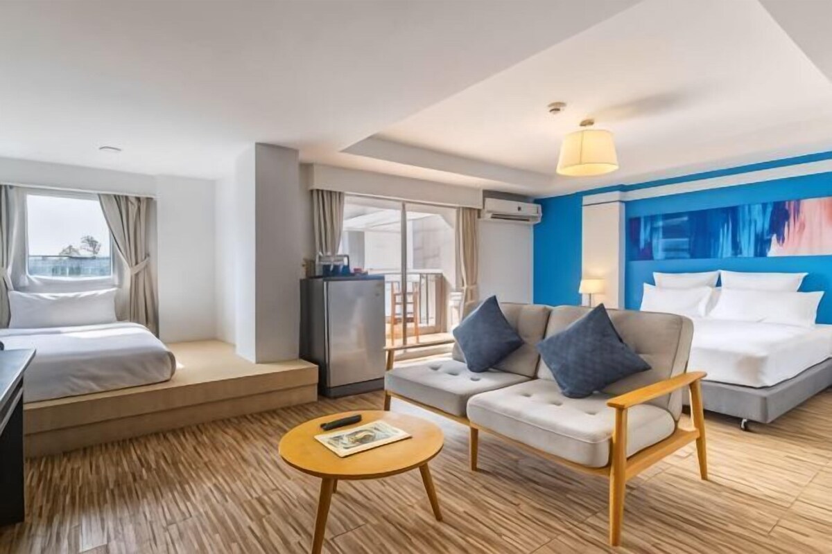 A hotel room with a bed, sofa, dining table, and a balcony with a view.