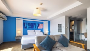 A modern hotel room with a bed, a sofa, a desk, and a large abstract painting on the wall. - Journeyhub Pattaya Central (Pattaya)