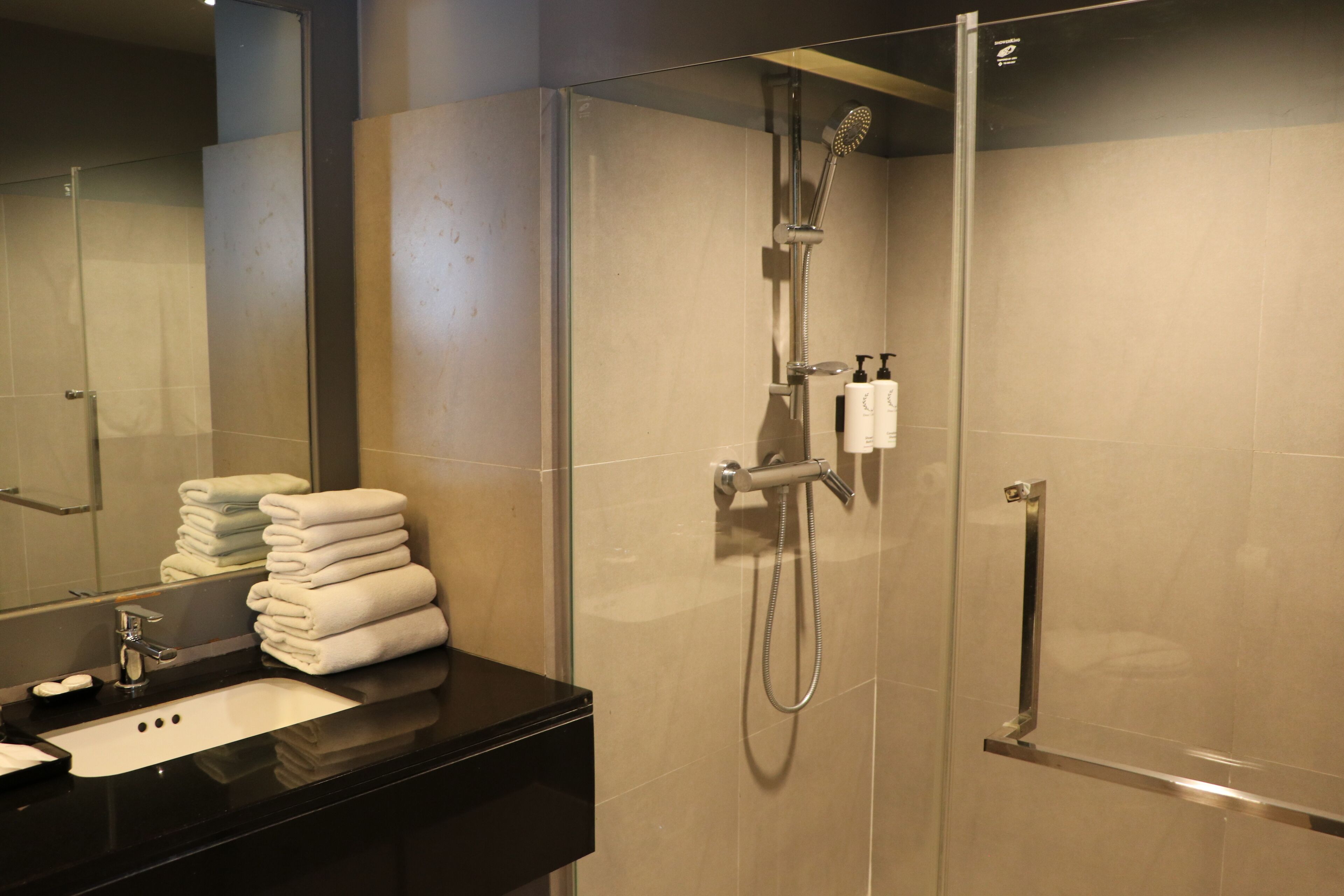 Un baño moderno con cabina de ducha de vidrio, encimera negra y toallas ordenadas.