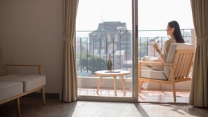 A room with a balcony, a sofa, a table with a bottle, and a chair. - Journeyhub Pattaya Central (Pattaya)
