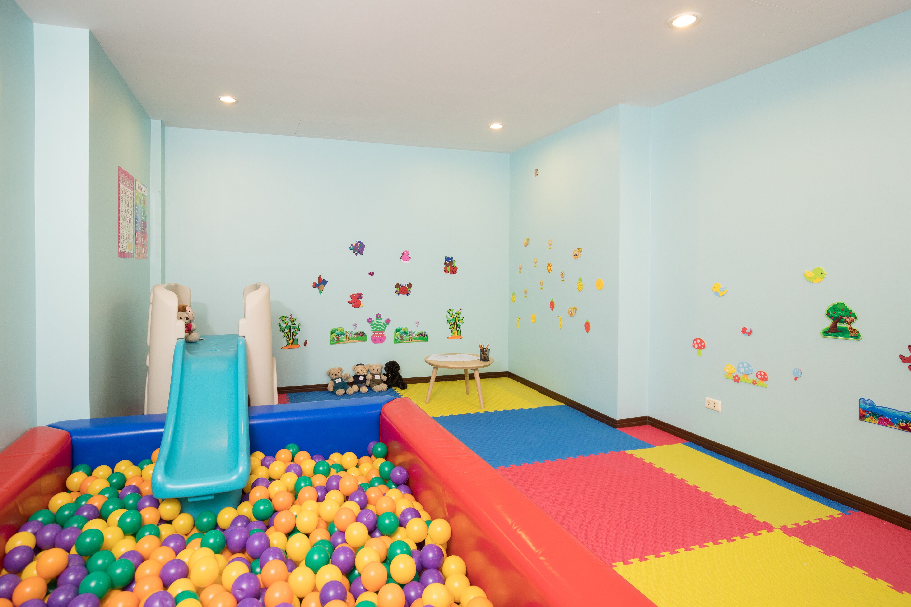 Zona de juegos infantiles con tobogán, piscina de pelotas y colchonetas de espuma.