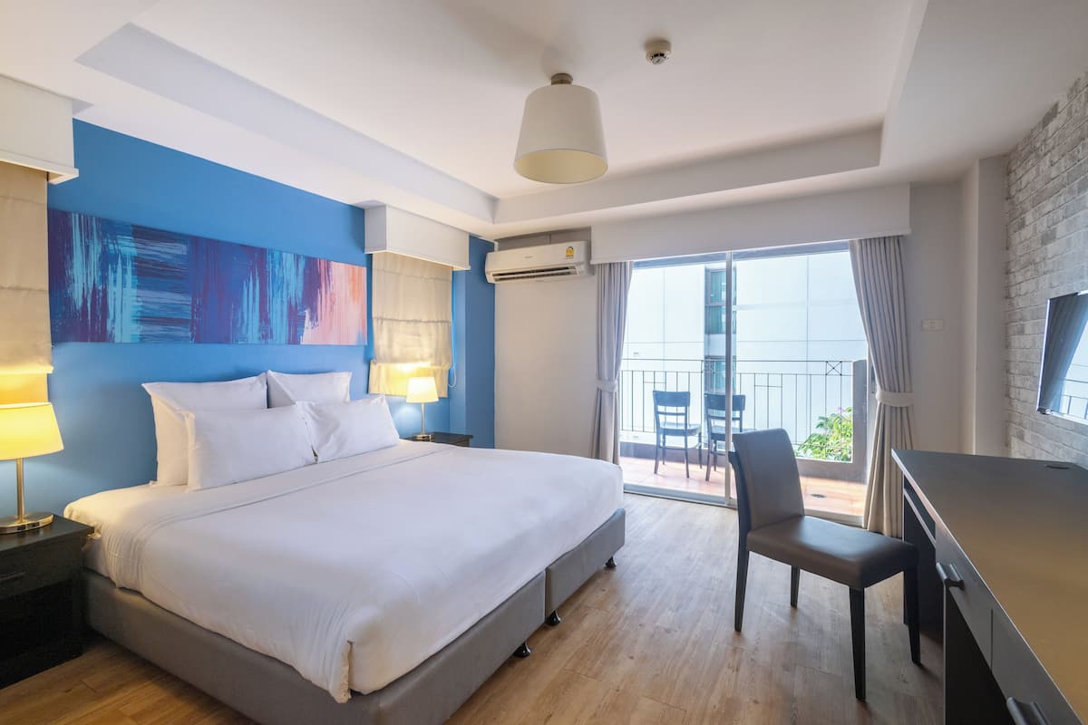 Ein Hotelzimmer mit einem großen Bett, einem Schreibtisch, einem Stuhl, einer Klimaanlage und Blick ins Freie.