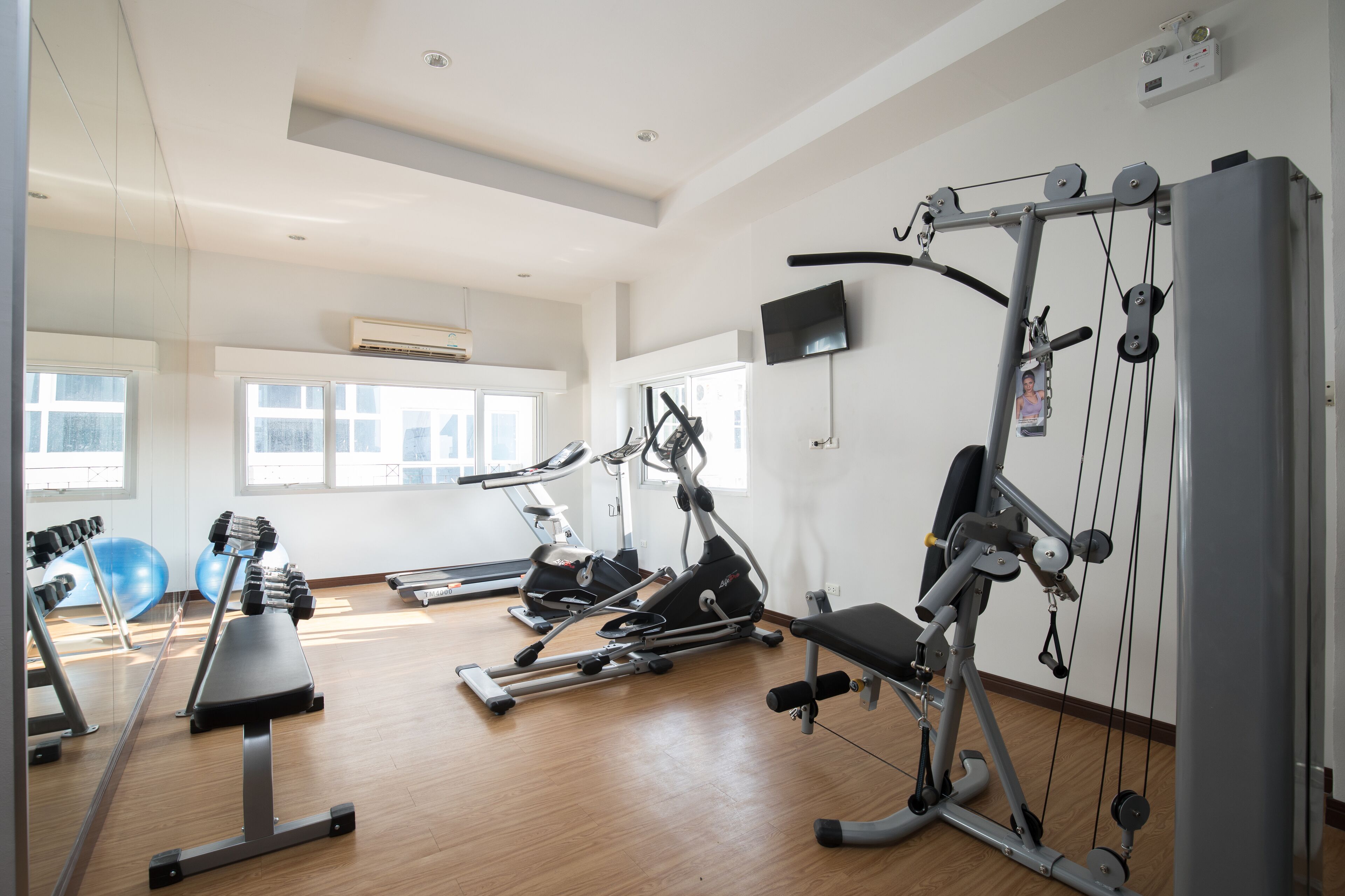 Ein Fitnessstudio mit Cardiogeräten, Kurzhanteln und einem Fernseher an der Wand.