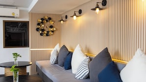 A modern living area with a sofa, pillows, a round table with a plant, and a wall-mounted light fixture. - Journeyhub Pattaya Central (Pattaya)