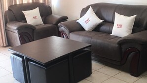 A living room with two brown leather sofas, each with a white pillow featuring "BJ&T" text, and a black coffee table in the center. - BJ&T Vacation Homes (Kasane)