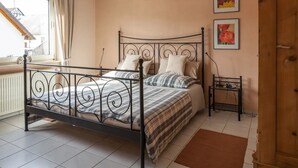 Une chambre à coucher avec un lit en métal, une table de chevet, un radiateur et une fenêtre avec des rideaux.