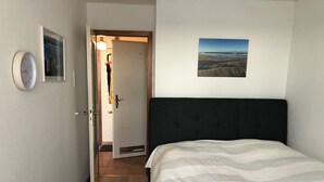 A hotel room with a bed, a clock, a door, and a framed picture on the wall.