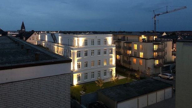 A multi-story building with illuminated windows, a visible staircase, and a crane in the background.