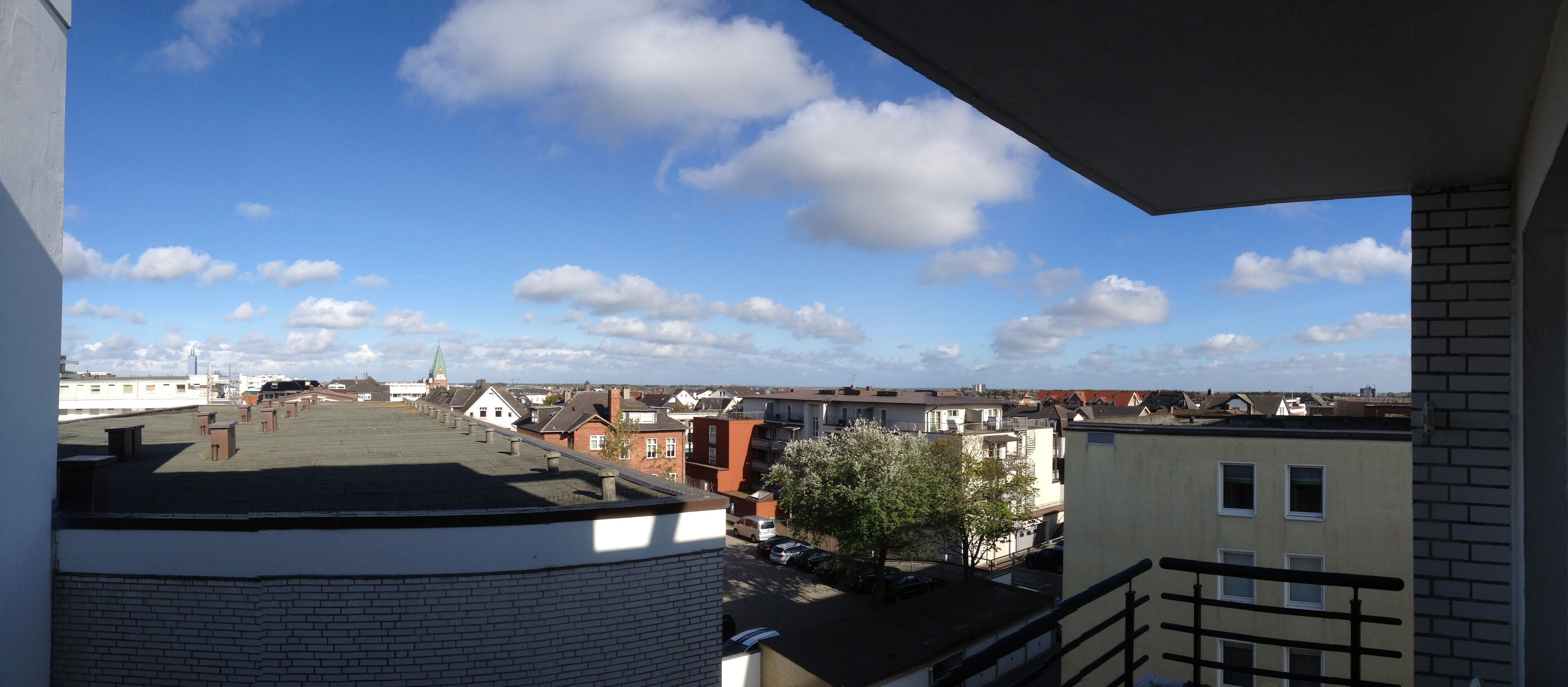A view from a balcony overlooking a residential area with a clear sky and scattered clouds.