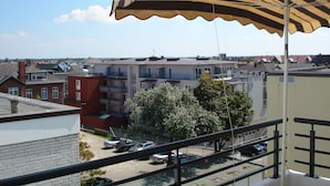 A balcony with a striped awning overlooking a residential area with multiple buildings and parked cars.