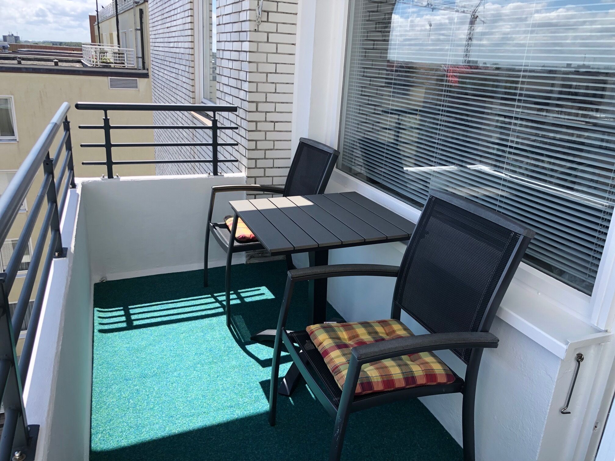 Un balcón con mesa y sillas, una ventana con persianas y vistas a la ciudad.
