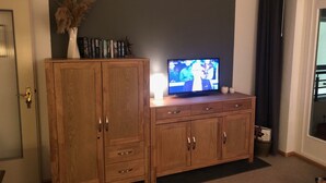 A living room with a wooden cabinet, a television, and a vase with dried flowers.