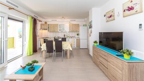 Une cuisine moderne avec des meubles de rangement en bois, un coin repas avec une table et des chaises, un téléviseur posé sur une console en bois et une petite plante en pot sur la console.