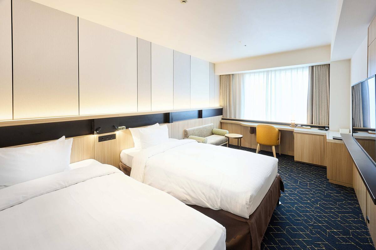 Una habitación de hotel con dos camas, un escritorio, una silla y un televisor.