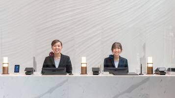 Two receptionists at a reception desk with laptops, a phone, and a tablet.
