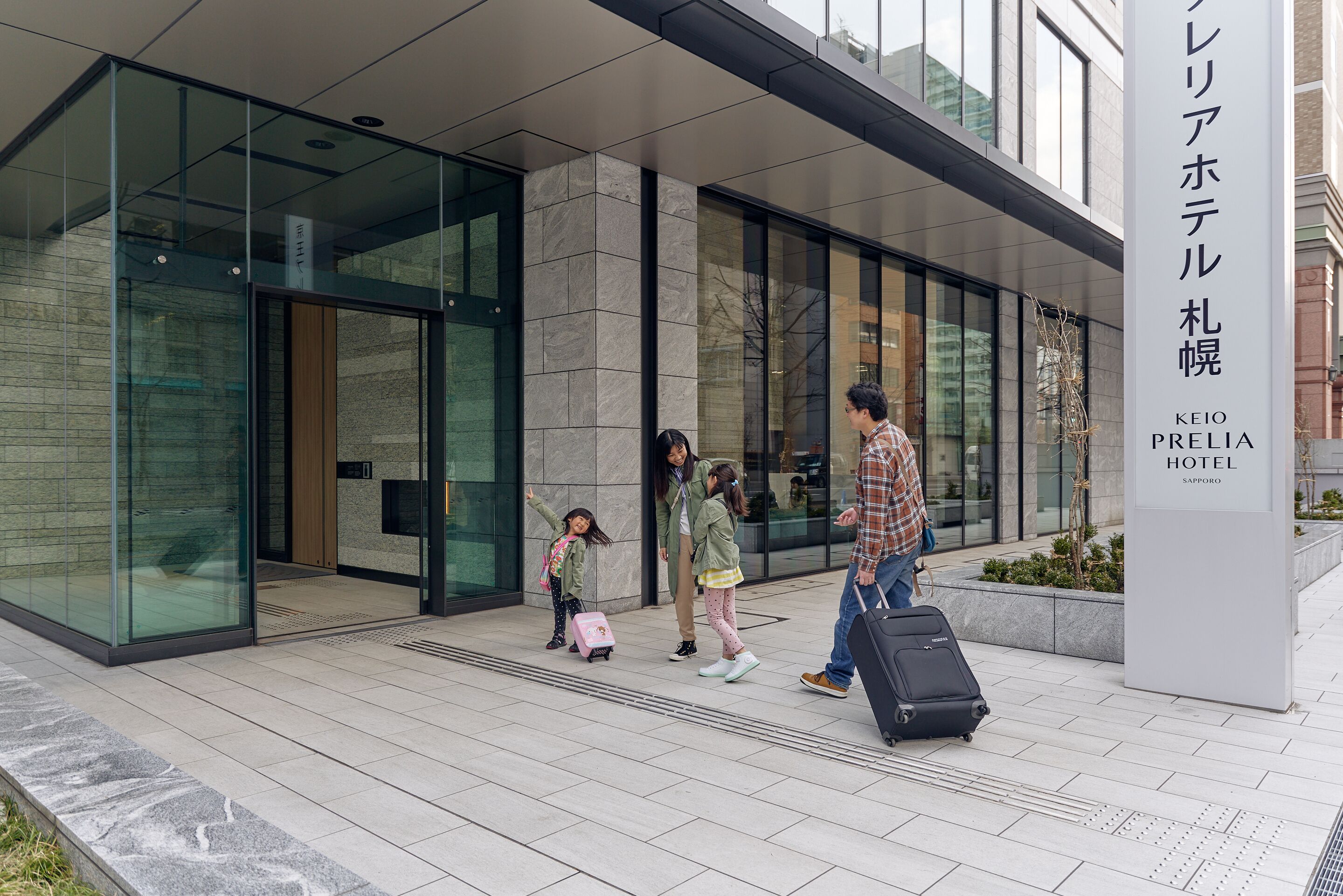 A modern hotel entrance with a clear glass facade, a signboard with hotel name, and a tiled pavement.