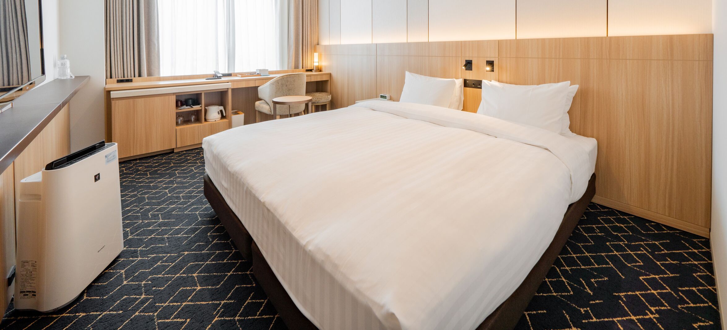 Een hotelkamer met een groot bed, een bureau met stoel, een bijzettafeltje en een prullenbak.