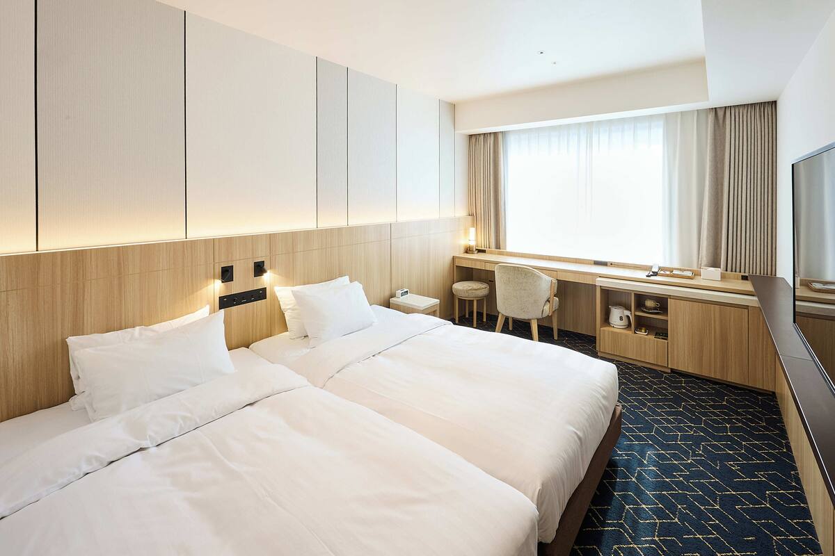Una habitación de hotel con una cama grande, un escritorio con una silla, televisión y ventana con cortinas.