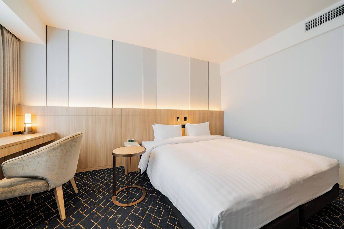Una habitación de hotel con cama, escritorio, silla y una pequeña mesa.