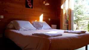 Ein Zimmer mit Holzboden, einem Bett, zwei Wandleuchten und einem Fenster mit Blick auf Grünflächen.