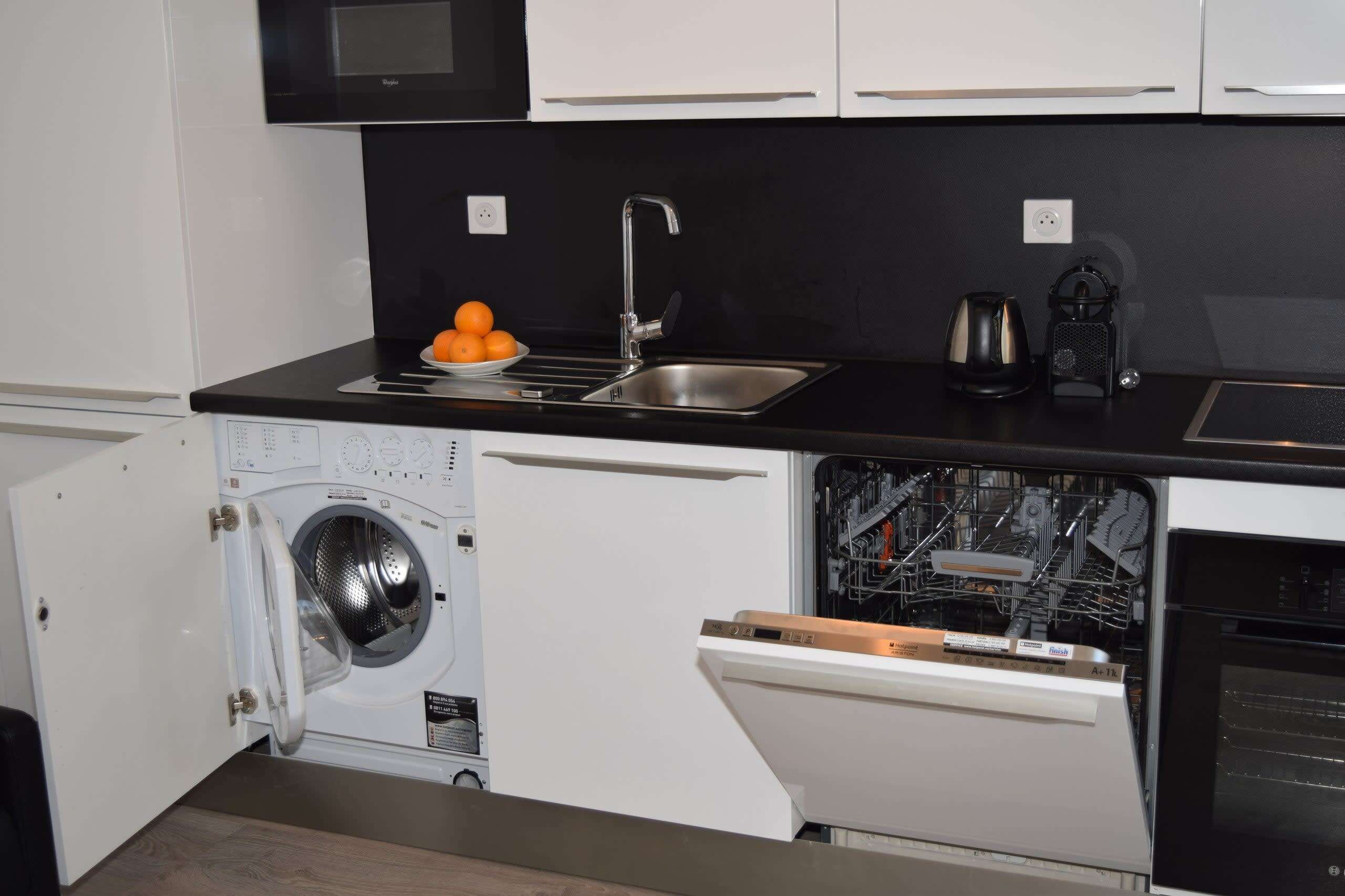 Een kleine keuken met een wasmachine, vaatwasser en een spoelbak met waterkoker.