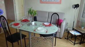 A dining area with a glass table set for four, surrounded by chairs, a sofa, and a small table with a lamp. - Cannes, 2 rooms Furnished 3 stars 10 mn from the Palais and the beach (Cannes)